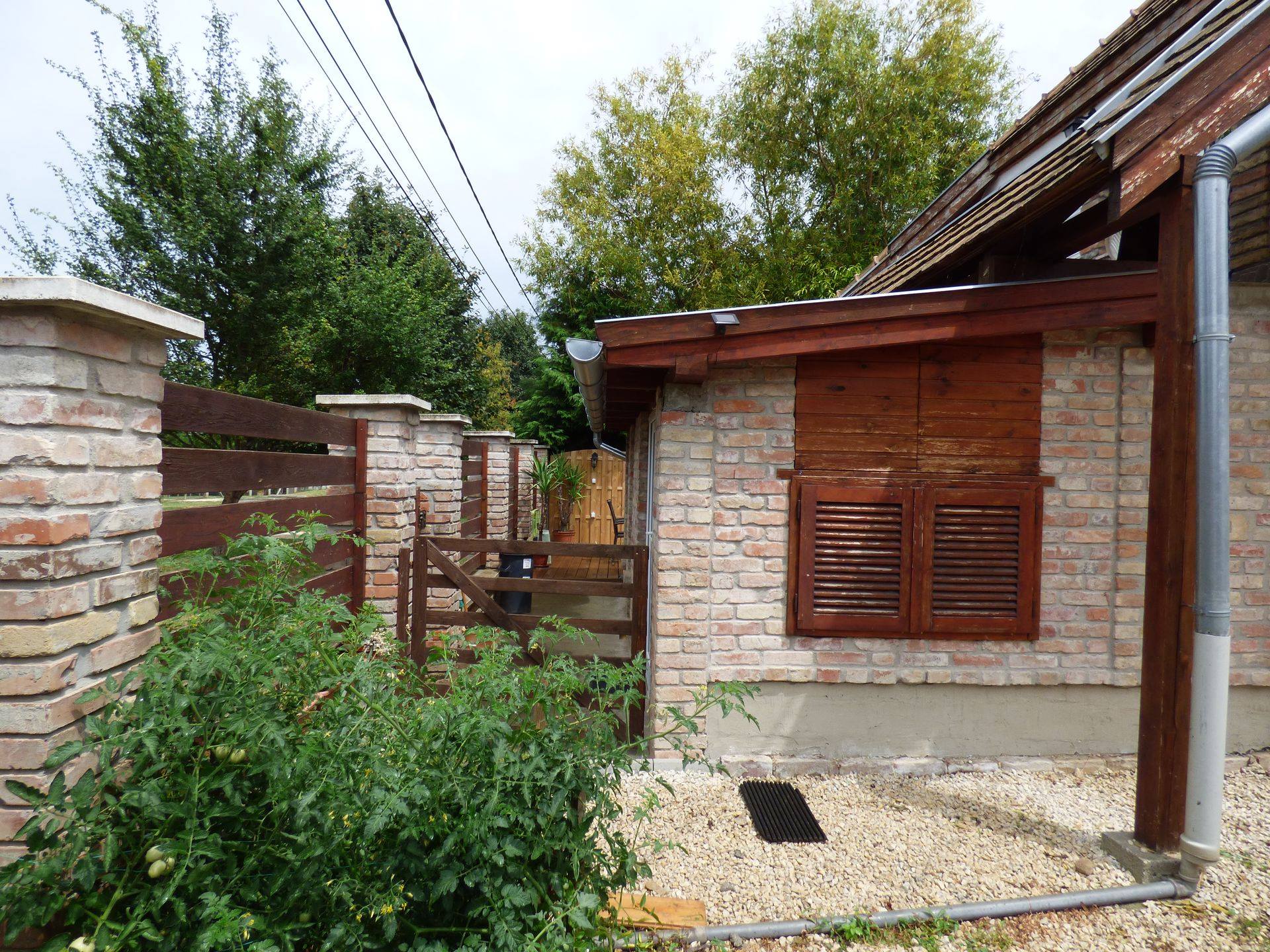 Az apartman oldalsó, téglafalas része fa zsalugáteres ablakkal és kavicsos járdával
